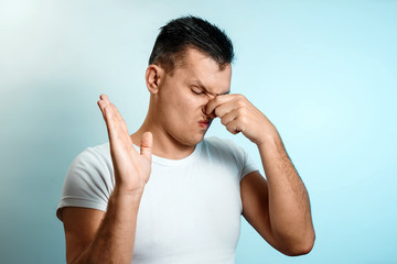 Wall Mural - Close-up portrait of a man, closes his nose with his hands. On a light background. The concept of bad smell, stench.