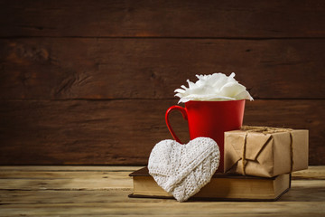 Wall Mural - Gift box, in a red cup white rose, heart and book on a wooden background