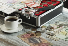 Different Collector's Coins And Banknotes, Cup Of Coffee And A Magnifying Glass