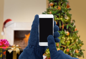 Wall Mural - closeup of man with gloves using the smart phone with a Christmas tree background at home