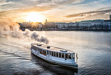 Steamboat On Alster Lake In Hamburg, Germany With Cityscape In Background During Sunset