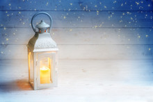 Christmas Background With A Lantern And Burning Candle Light On Rustic White Wood, Blue Sky With Stars, Copy Space