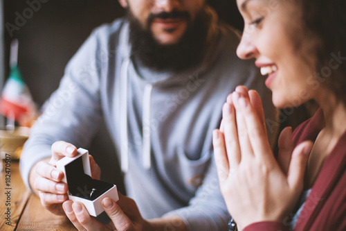 Fotografía A man with a beard asks to marry his happy and surprised girl in a cafe, gives a diamond ring