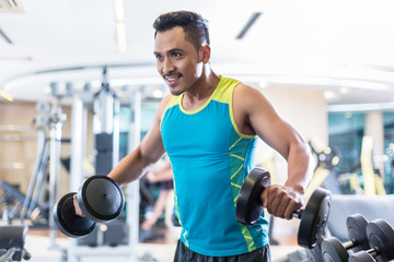 Portrait of a handsome determined young man exercising with dumbbells during upper-body workout routine in a modern fitness club