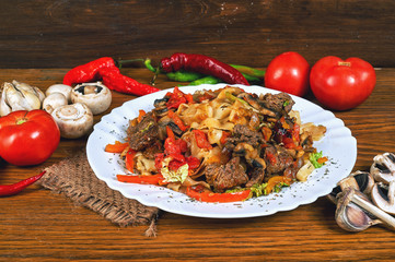 Pasta with roasted meat and vegetables on wooden table