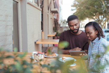 Wall Mural - Young African couple browsing online at a sidewalk cafe