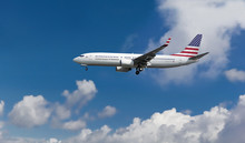 Commercial Airplane With American Flag On The Tail And Fuselage Landing Or Taking Off From The Airport With Blue Cloudy Sky In The Background