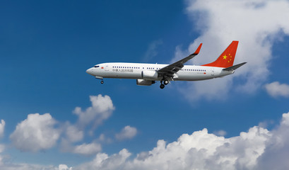 Commercial airplane with Chinese flag on the tail and fuselage landing or taking off from the airport with blue cloudy sky in the background