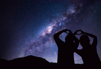 People makes heart symbol by hand with Milky Way and night sky on background.