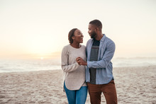 Young African Couple Walking On A Beach At Sunset Laughing 