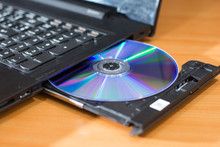 DVD ROM Inserted In Laptop Computer On Wooden Texture Background