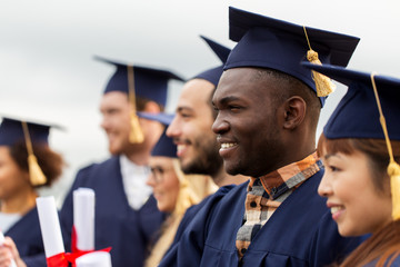 happy students in mortar boards with diplomas