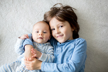 happy brothers, baby and preschool children, hugging at home on white blanket