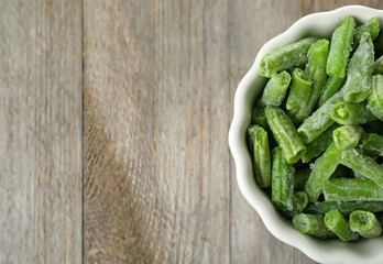 Canvas Print - White bowl with frozen green beans on wooden background