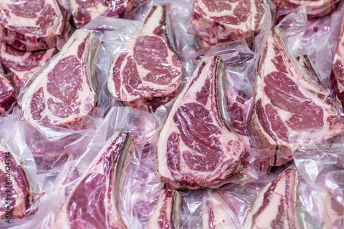 Fotografía Fresh tasty raw beef steaks with bone wrapped in vacuum plastic packing at market or shop