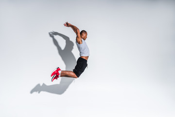 side view of young african american sportsman jumping on grey