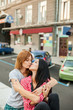 © luckyphoto - Two young girlfriends hugging, kissing and sitting near road. one brunette girl in red plaid shirt and black trousers, another redhead girl in gray shirt and blue skirt. concept of sincere friendship