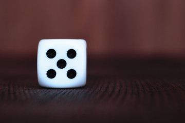 Wall Mural - Single white plastic dice on brown wooden board background. Six side cube with black dots. Number 5.