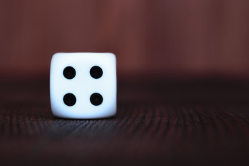 Wall Mural - Single white plastic dice on brown wooden board background. Six side cube with black dots. Number 4.