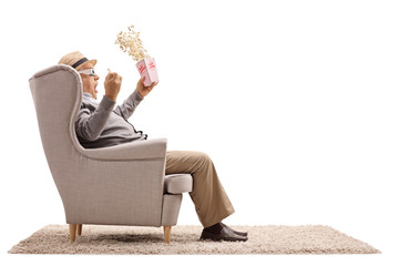 Poster - Terrified senior with a popcorn box and 3D glasses seated in an armchair