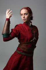 portrait of a red haired girl wearing medieval warrior outfit, studio background.