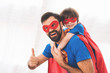Father and son in the red and blue suits of superheroes. On their faces are masks and they are in raincoats.