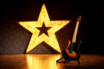 An electric guitar on the background of a large electric star with luminous bulbs.