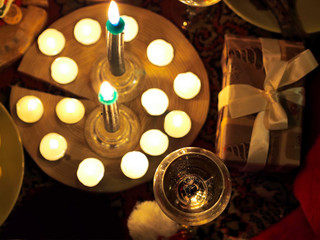 Сhampagne in a glss in cozy Christmas atmosphere with two candles, santa claus' hat and gift box. Top view. Shallow DOF, focus is on the glass content.