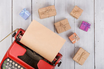 Poster - Holidays concept - red typewriter with blank craft paper, gift boxes on white wooden background