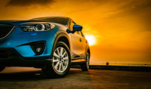 Blue Compact SUV Car With Sport And Modern Design Parked On Concrete Road By Sea Beach At Sunset. New Shiny SUV Car Drive For Travel On Summer Vacations With Road Trip. Front View Of Electric Car.