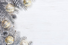 Silver Christmas Tree Branches Decorated With Glowing Light Garlands And Pine Cones On White Wooden Background