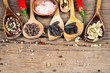 Nahaufnahme von fünf Kochlöffeln aus Holz mit verschiedenen exotischen Gewürzen und zwei roten Chilischoten auf rustikalem Holzhintergrund und Textfreiraum
