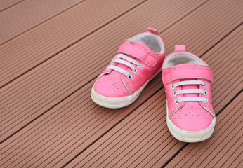 Pair of pink baby leather sneakers on wood plank background.