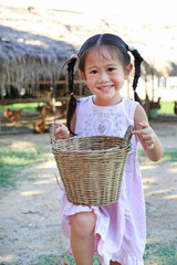 Wall Mural - Adorable little asian girl holding a basket with eggs outdoors in the farms.