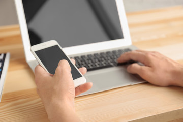 Wall Mural - Man using cell phone and laptop on table, closeup