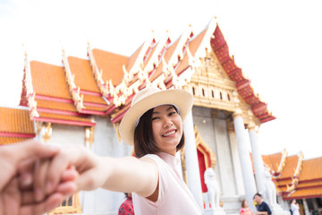 Asian tourist women in hat leading man hand to travel at marble temple