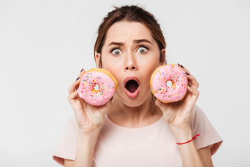Wall Mural - Close up portrait of a shocked pretty girl holding donuts