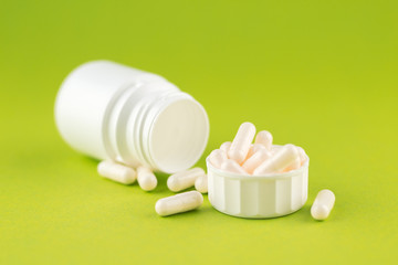 Close up white pill bottle with spilled out pills and capsules in cap on pear yellow background with copy space. Focus on foreground, soft bokeh. Pharmacy drugstore concept