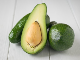 One cut and two whole avocados on white wooden table.