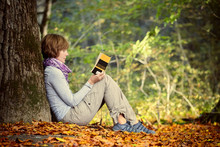 A Girl Is Reading A Book Sitting By A Tree