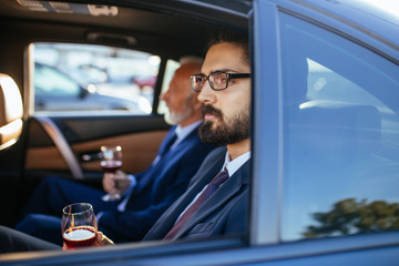 Senior businessman and his assistant sitting in limousine.