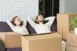 Happy couple relaxing on sofa with boxes, relaxed man and woman resting on couch hands behind head on moving day, dreaming of future in new own home, delivery service for easy move concept