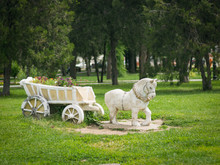 Flowerbed Of Figurines Horse With Cart In The City Park.