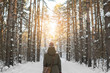 © PAstudio - Woman walks a winter forest with the morning light streaming through the trees and illuminating the pine trees behind.