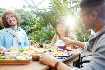 Happy friends gathered by breakfast or dinner in orangery or in the garden