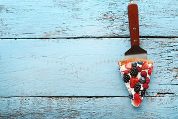 Wall Mural - Slice of tart with berries on blue wooden table