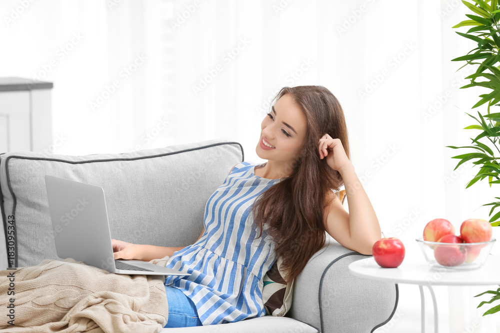 Young woman using laptop while sitting on cozy sofa indoors