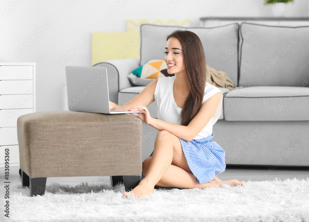 Young woman using laptop while sitting on soft carpet indoors