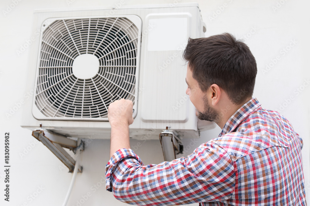 Handsome man repairing air conditioner outdoors