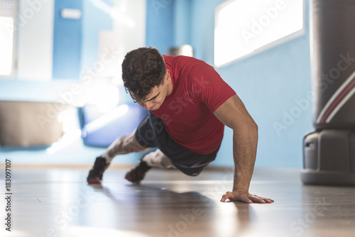 Cuadros en Lienzo Jove hombre entrena flexiones a una mano en el suelo del gimnasio